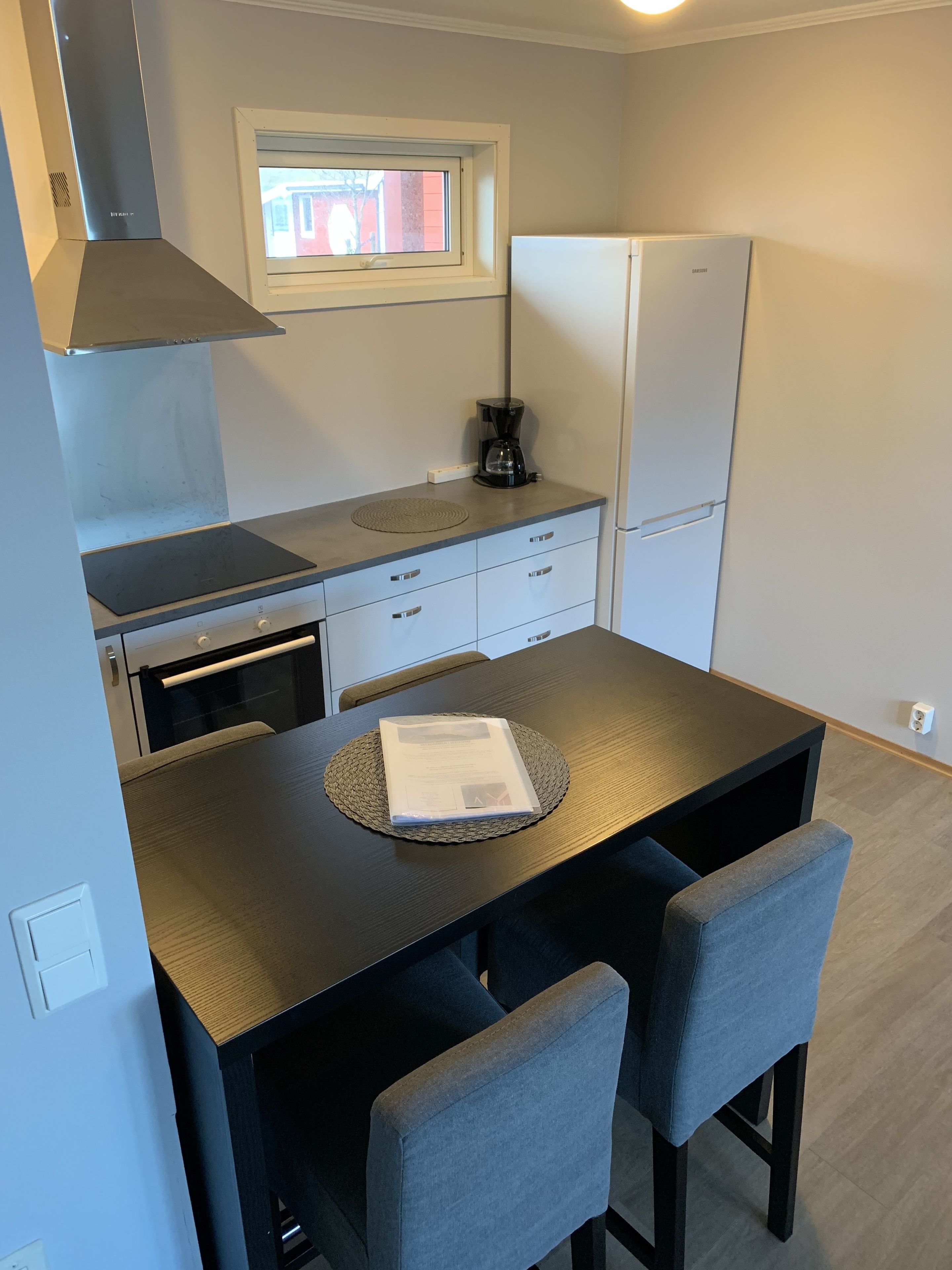 A compact kitchen with a built-in oven, a coffee maker, and a refrigerator. There is a window above the sink and a small countertop.