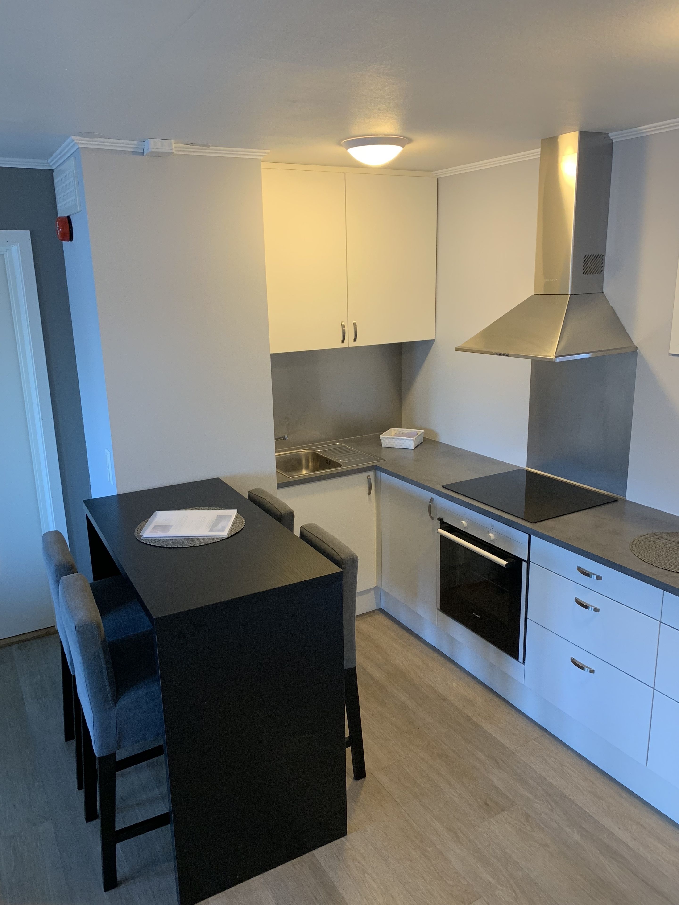 Een kleine keuken met een eettafel, stoelen, een inbouwoven en witte kastjes.