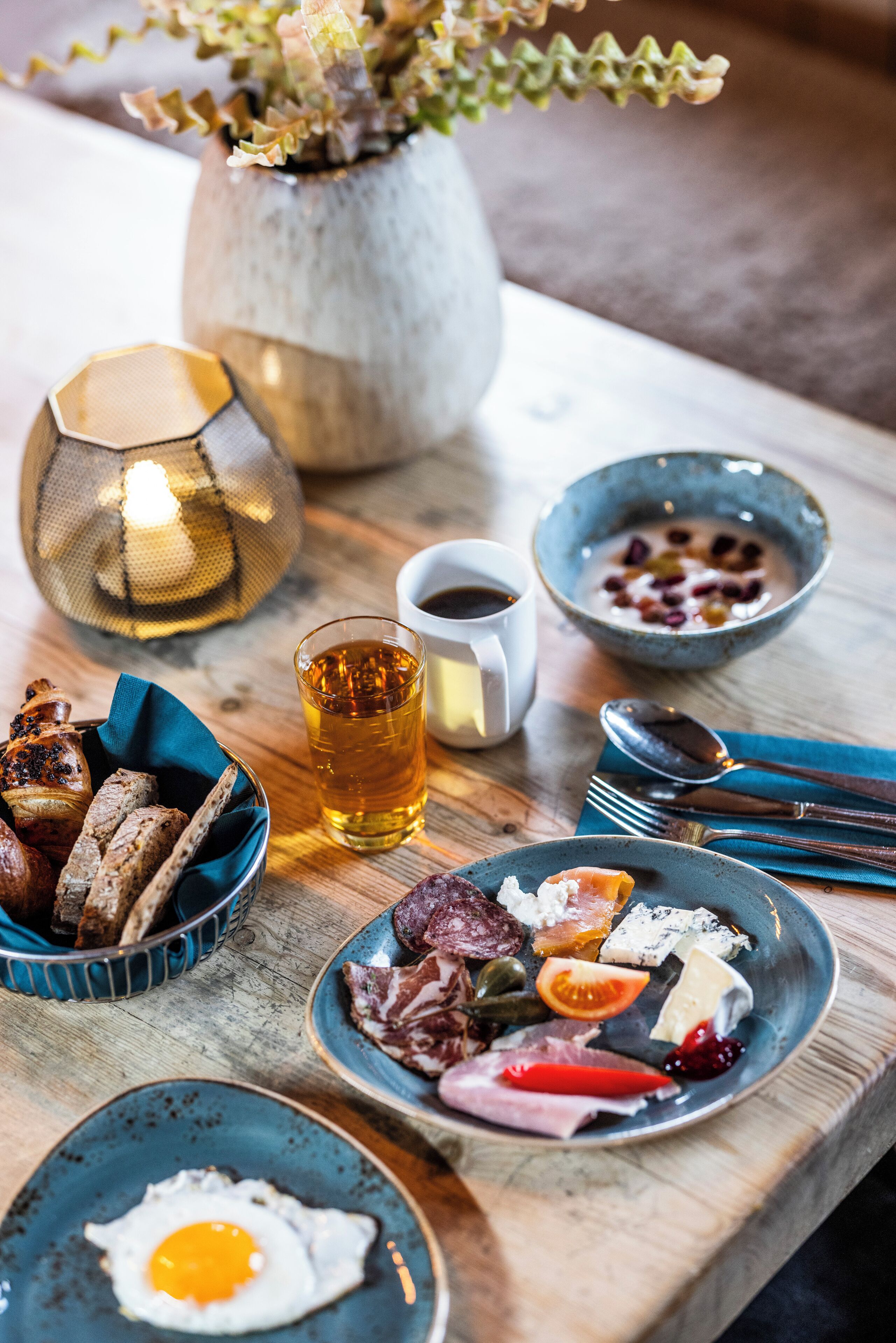 Une table dressée pour le petit-déjeuner, avec différents plats, notamment des œufs, de la viande et un saladier de fruits.