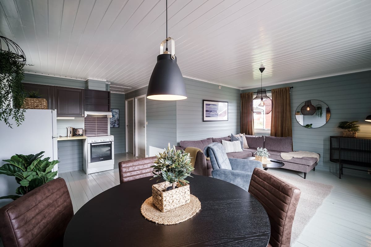 A modern living room with a dining table, sofas, and a kitchen area.