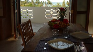 A dining table with a fruit bowl, glasses, and cutlery, overlooking a beach with palm trees. - Kamili View Apartment in Zanzibar (Kiwengwa)