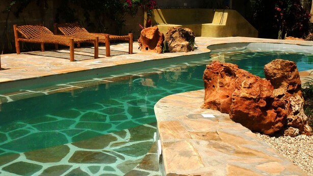 A clear swimming pool with a stone edge, lounge chairs, and a rock feature. - Kamili View Apartment in Zanzibar (Kiwengwa)