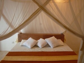 A bed with a canopy, white pillows, and a wooden headboard. - Kamili View Apartment in Zanzibar (Kiwengwa)