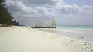 A beach with a boat with sails, clear sky, and calm sea. - Kamili View Apartment in Zanzibar (Kiwengwa)
