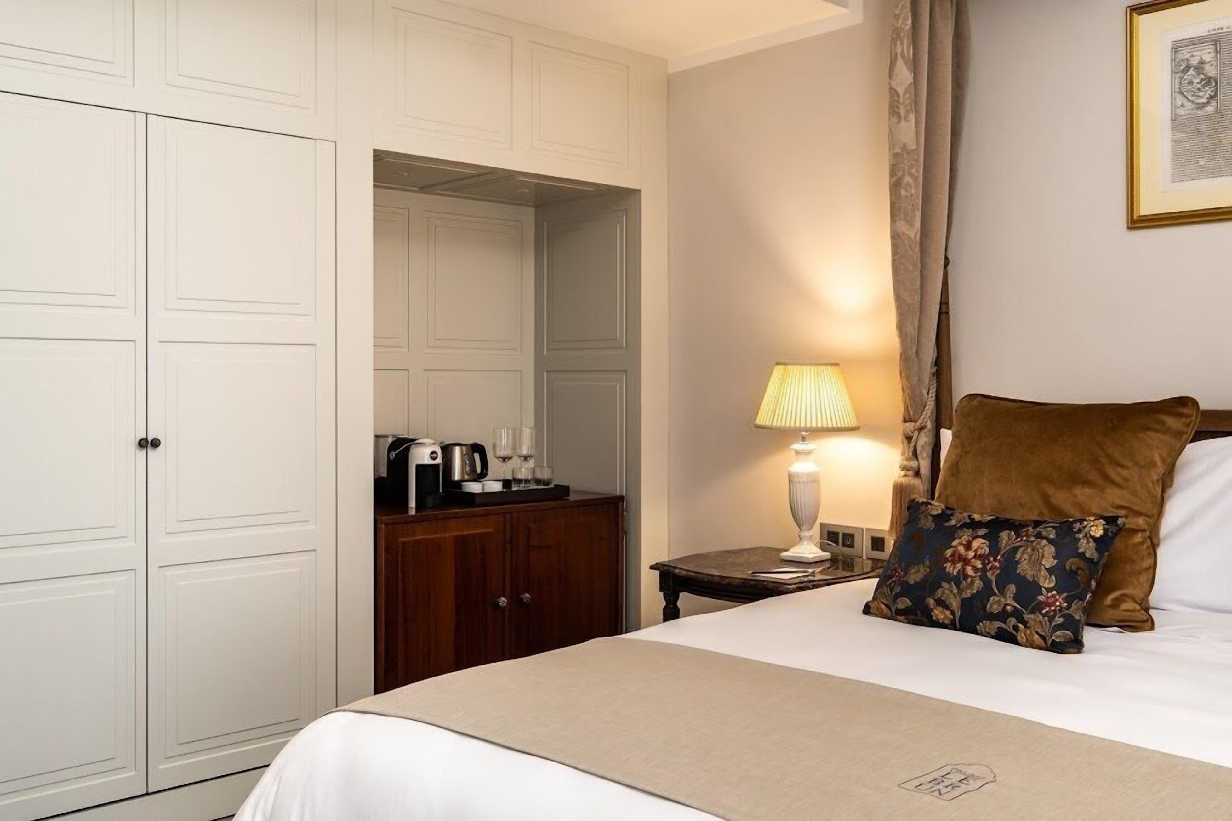 A hotel room with a bed, a nightstand, a lamp, a wooden dresser, and a wardrobe.
