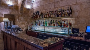 A bar area with a stone wall backdrop, a wooden counter, and shelves stocked with various liquor bottles. - Palais Le Brun (Valletta)