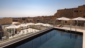 A rooftop pool with lounge chairs and umbrellas, overlooking a cityscape. - Palais Le Brun (Valletta)