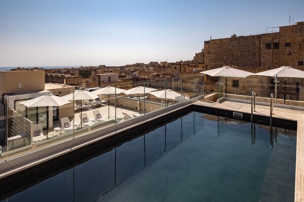 A rooftop pool with lounge chairs and umbrellas, overlooking a cityscape. - Palais Le Brun (Valletta)