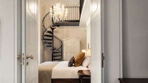 A bedroom with a bed, a nightstand, a chandelier, a staircase, and a door. - Palais Le Brun (Valletta)