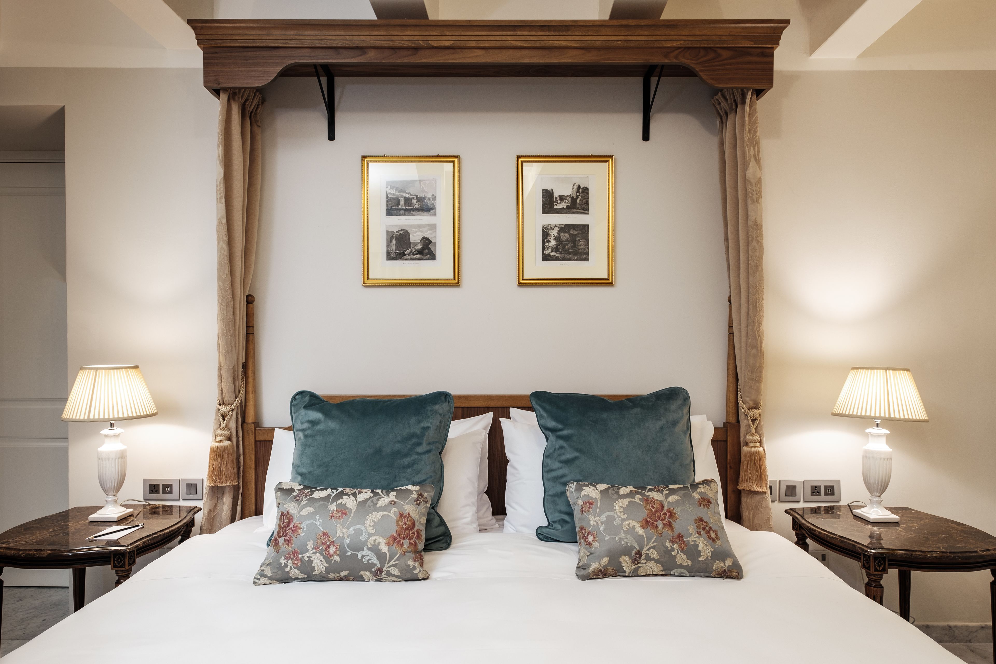 Quarto de hotel com uma cama grande, duas mesas de cabeceira, um painel de madeira na cabeceira e duas fotos emolduradas na parede.