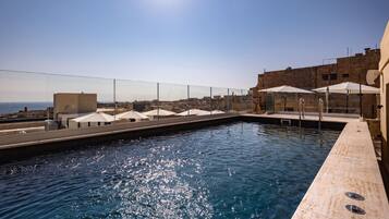 A rooftop pool with clear blue water, surrounded by a glass barrier and umbrellas.
