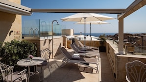 A rooftop terrace with sun loungers, umbrellas, and a glass balustrade overlooking the sea. - Palais Le Brun (Valletta)