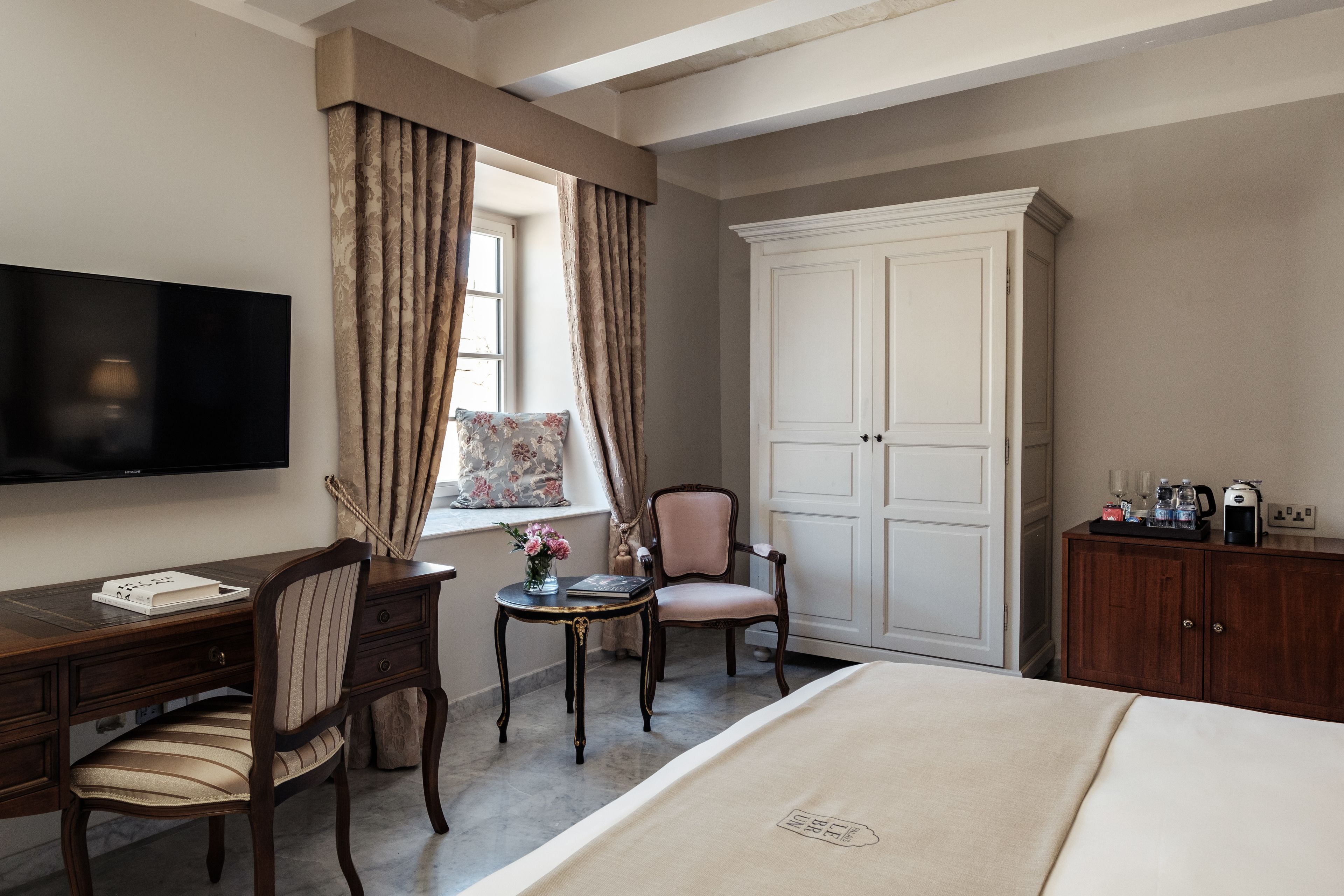 Habitación de hotel con cama, escritorio con silla, televisión, armario y ventana con cortinas.