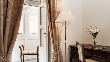Una habitación con una silla de madera, un escritorio con una lámpara y un jarrón de flores.