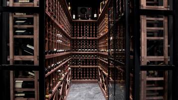 Une cave à vin avec des rangées de bouteilles de vin disposées sur des étagères en bois, un couloir central et un mur de verre sur l’un des côtés.
