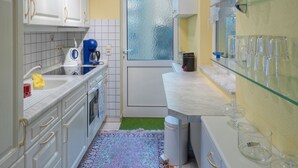 Een compacte keuken met witte kastjes, een koffiezetapparaat en een glazen displayplank.