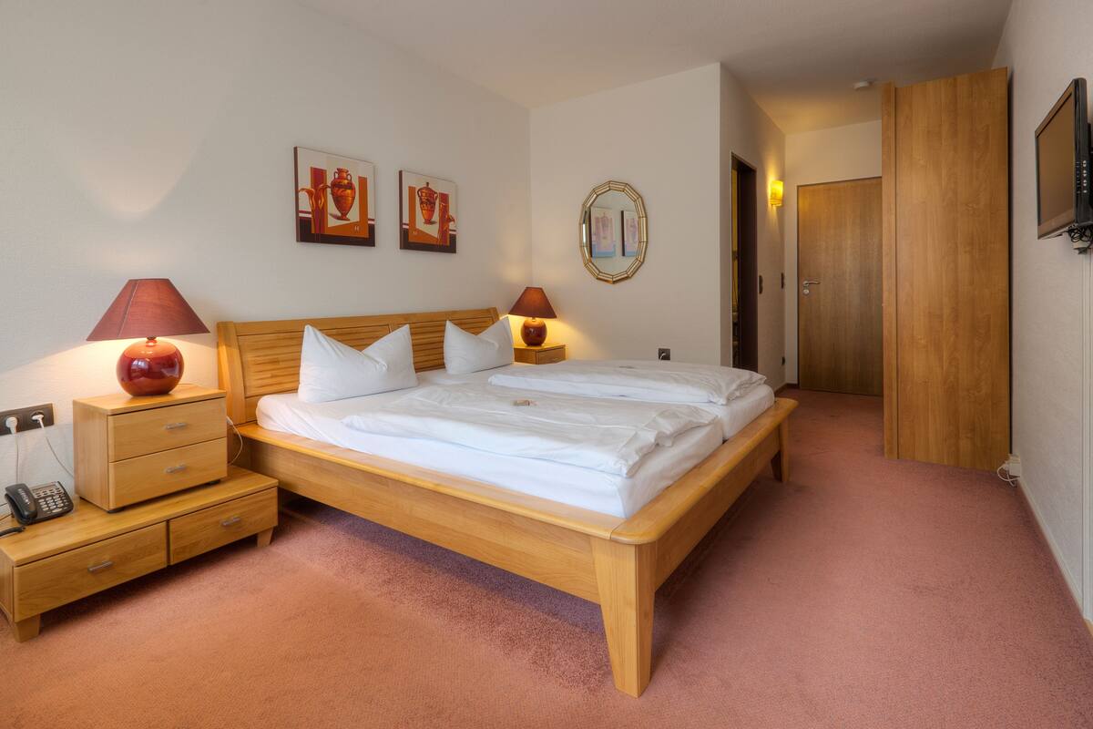 Un dormitorio con cama de madera, lámparas de noche, una mesita de noche y un teléfono.