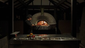 Un four à pizza en briques installé dans un espace extérieur abrité, avec un comptoir en métal et divers ustensiles de cuisine.