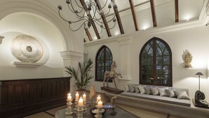 Un hall d’entrée spacieux avec un plafond haut, un lustre, une grande table ronde décorée de bougies et un coin salon comprenant un canapé et des fauteuils.
