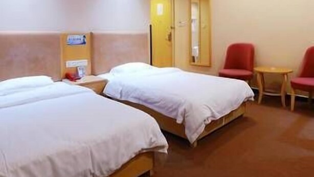Habitación de hotel con dos camas, una mesita, dos sillas rojas y un equipo de aire acondicionado en la pared.