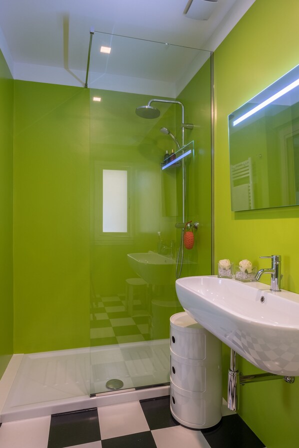 A modern bathroom with a green wall, a white sink, and a glass shower enclosure.