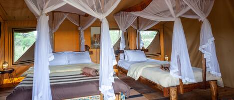 A room with two beds, each with a canopy, wooden flooring, and a view of greenery outside.