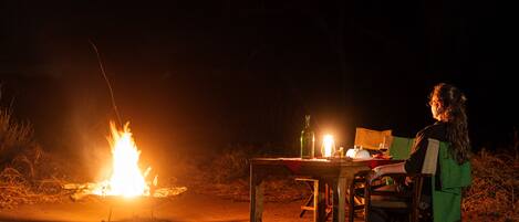 A person sitting at a table with a campfire in the background.