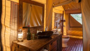 Un baño en una carpa pequeño y bien iluminado, con tocador de madera, un espejo grande, un lavamanos y un inodoro.
