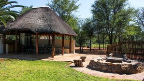 A thatched-roof pavilion with outdoor seating, surrounded by a stone fire pit and a fenced area. - Zingela Nature Reserve - Doornstock Lodge (Blouberg)