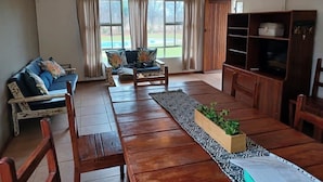 A spacious living room with a wooden floor, a sofa set, a coffee table, a TV stand, and a ceiling fan. - Zingela Nature Reserve - Doornstock Lodge (Blouberg)