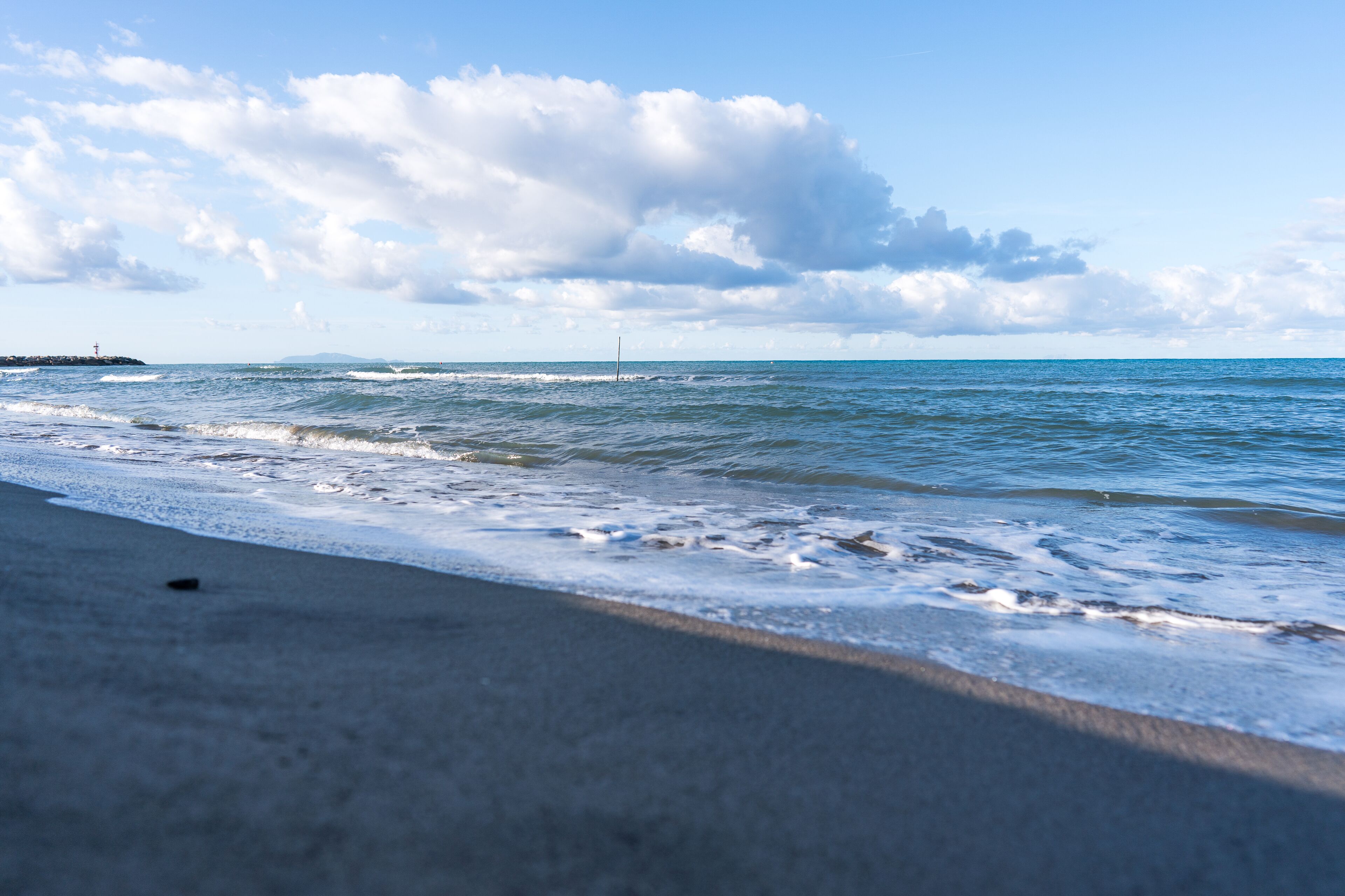 A beach with waves, a lighthouse in the distance, and a clear sky.