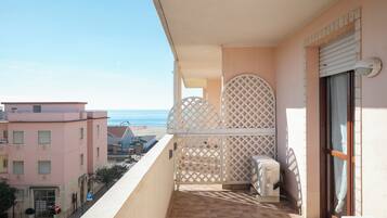 Un balcone con vista sulla spiaggia, un parapetto in legno chiaro e un edificio dalla facciata rosa.