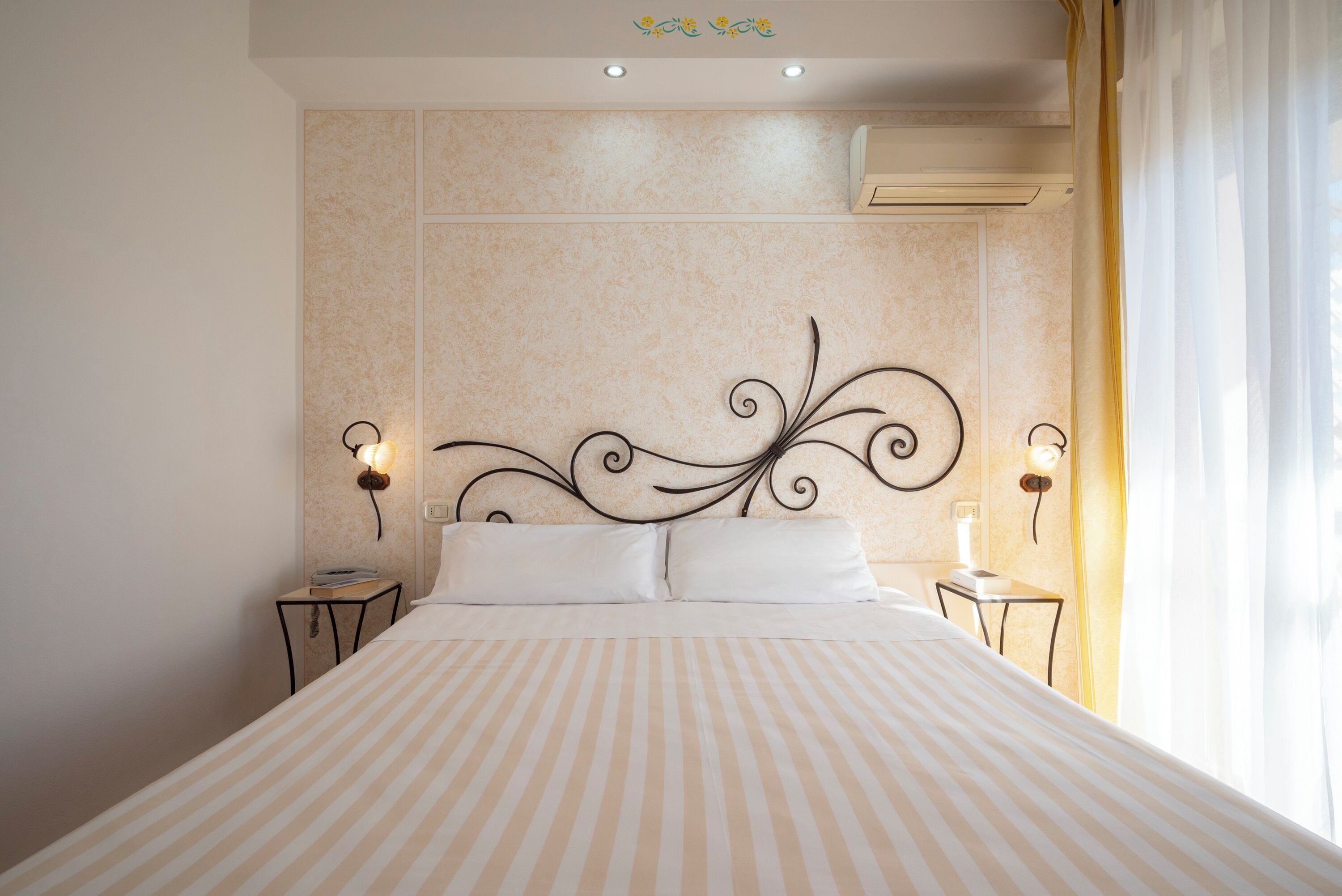 Una camera d'albergo con un letto grande, due comodini, una testiera decorativa e un condizionatore d'aria.