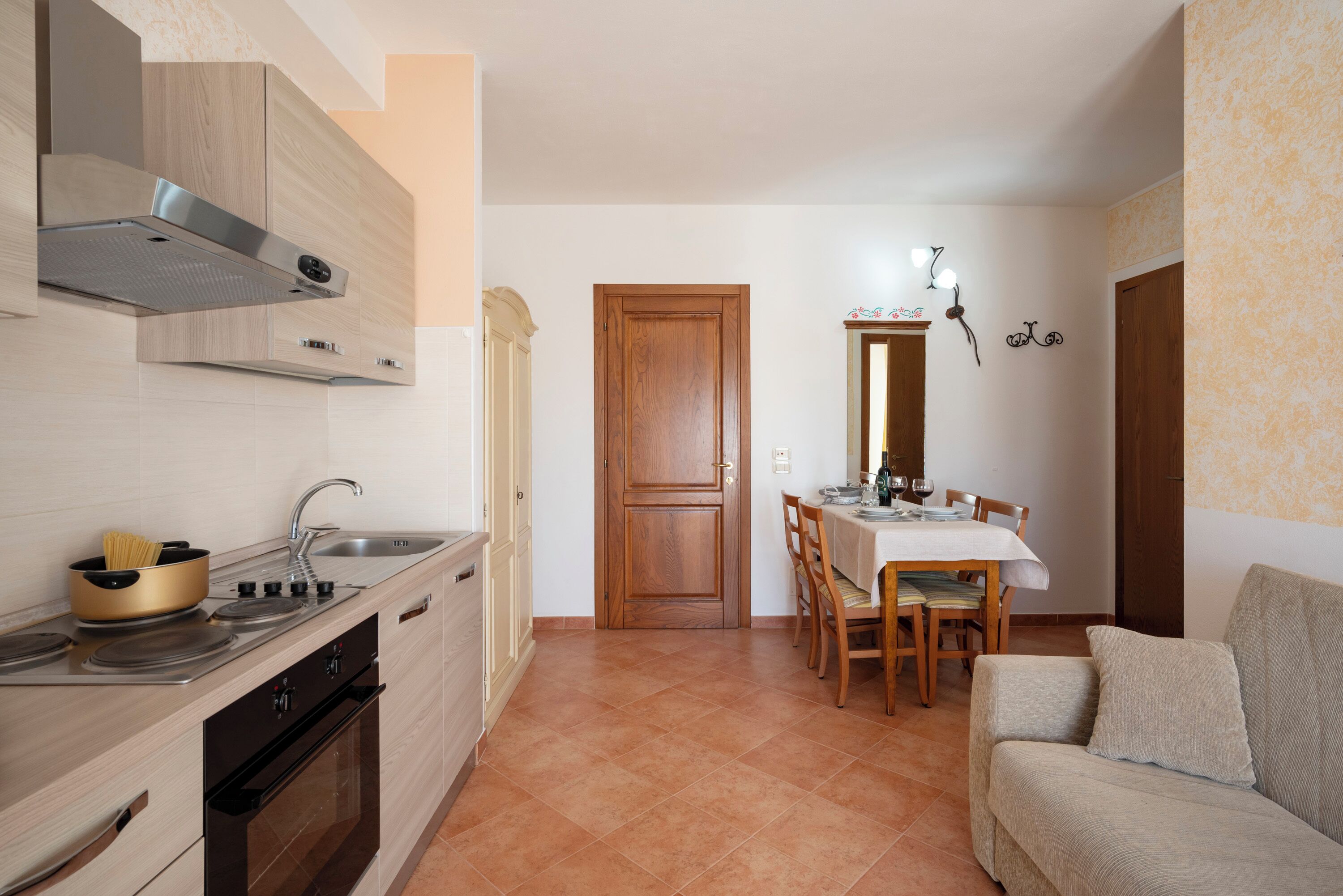 A compact kitchen with a stove, sink, and oven, a dining area with a table and chairs, and a sofa in a living area.