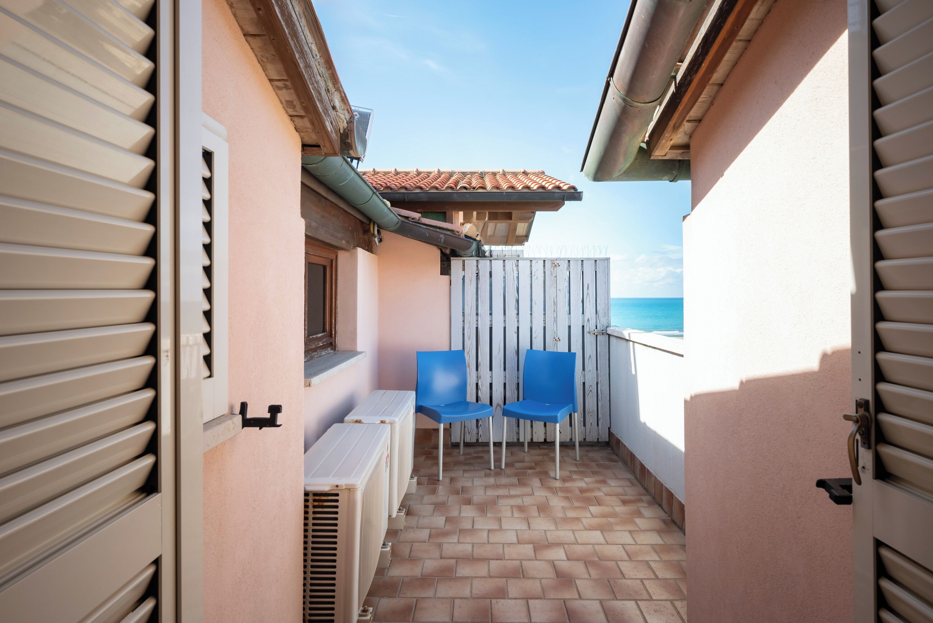 A balcony with two blue chairs, a white radiator, and a view of the sea.