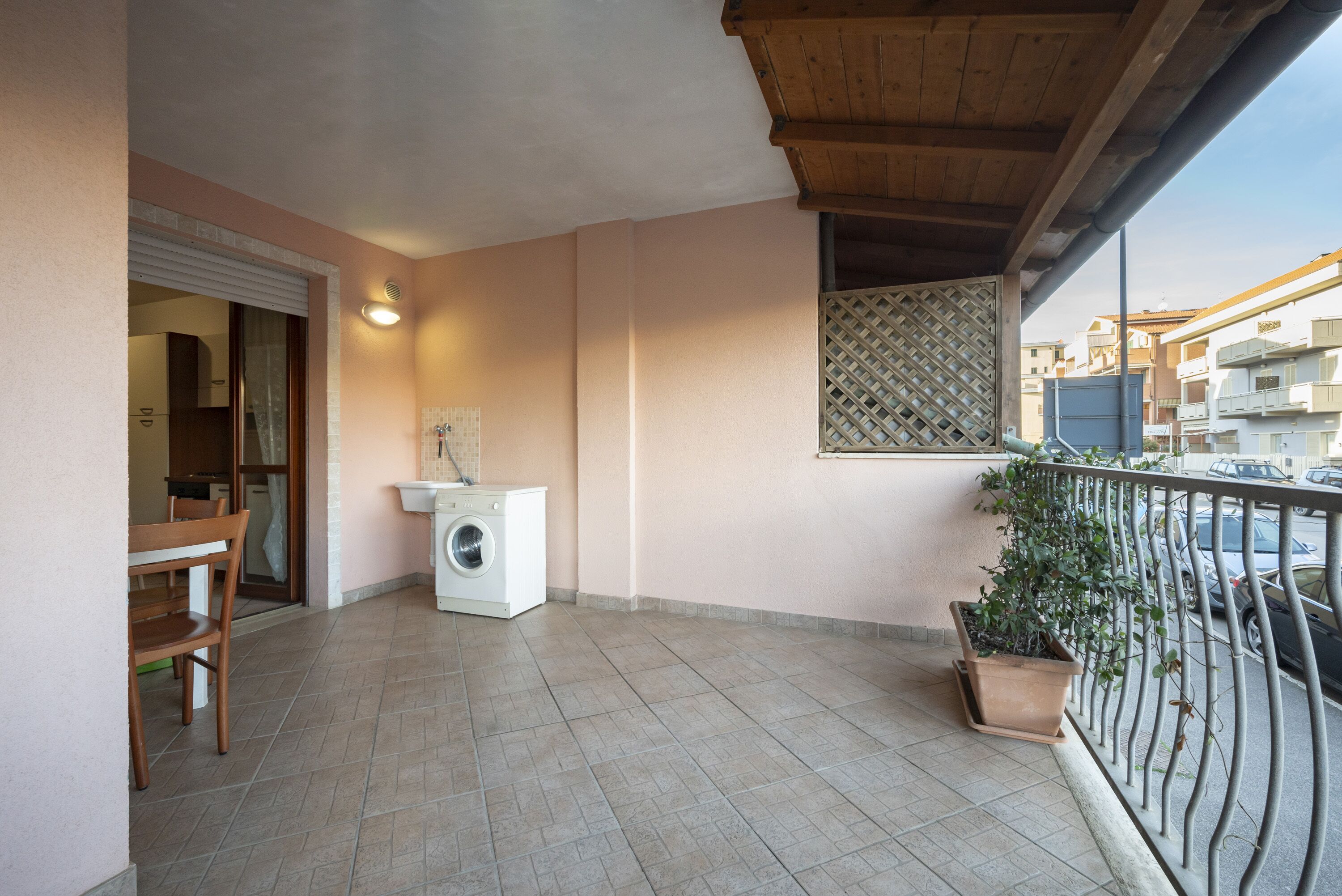 Een balkon met een wasmachine, een plant in pot en uitzicht op de straat.