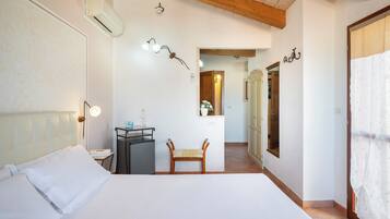 Ein Schlafzimmer mit einem Bett, Nachttisch und einem Sessel. An der Wand befindet sich ein Spiegel und eine Tür zu einem anderen Raum.