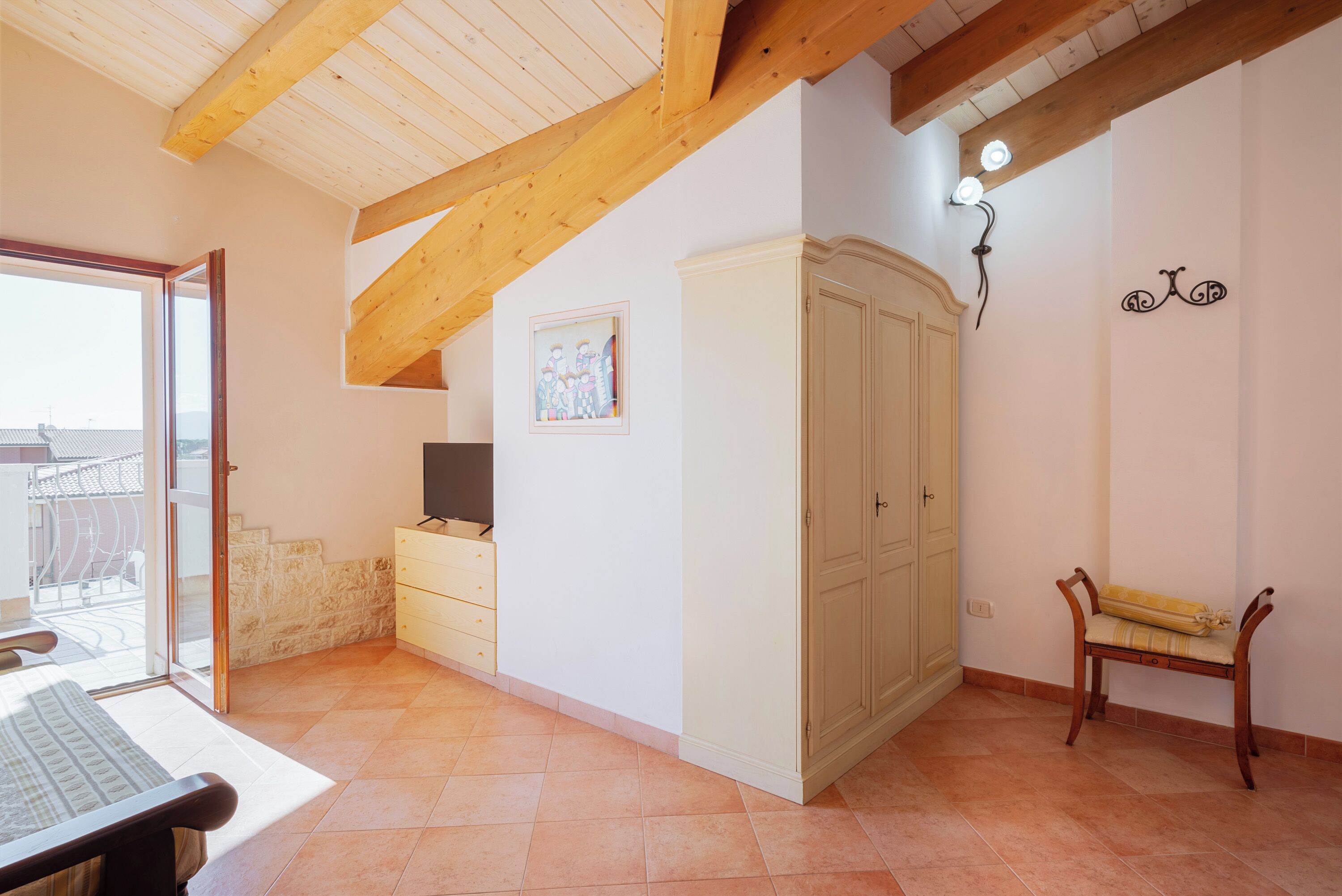Quarto com teto de madeira, guarda-roupa, um banco e uma pequena mesa.