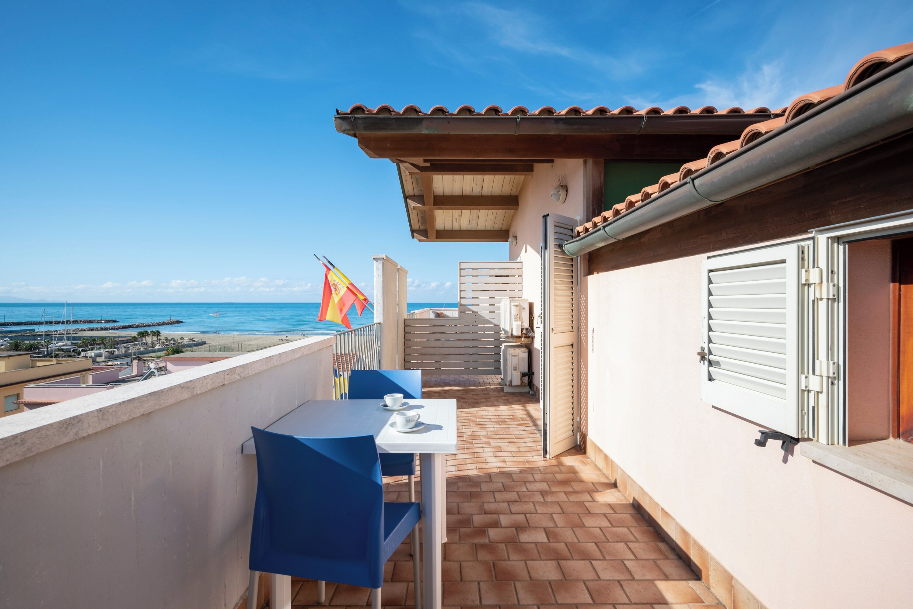 Un balcone con tavolo e sedie, una bandiera e vista sul mare.