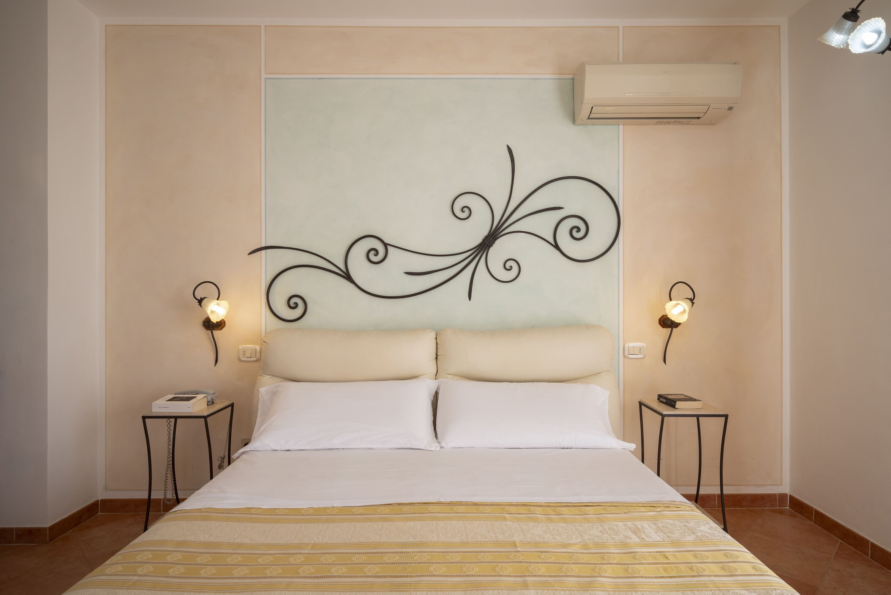 Une chambre d’hôtel avec un grand lit, deux tables de chevet, une tête de lit décorative et un appareil de climatisation.