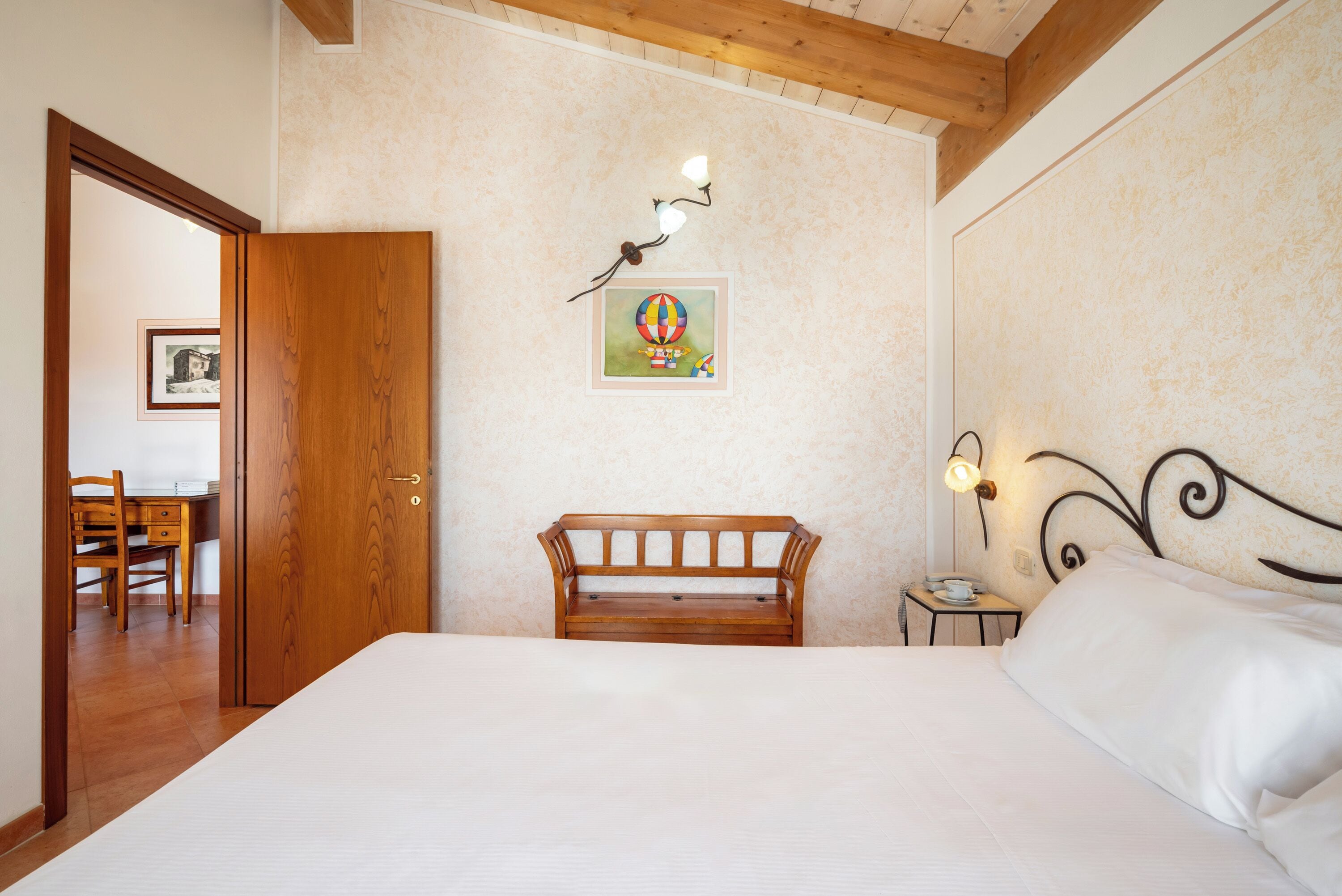 A bedroom with a wooden bed, a nightstand, a wall-mounted lamp, and a framed picture.
