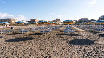 Ein Strand mit Liegestühlen und Sonnenschirmen, im Hintergrund Gebäude und ein klarer Himmel.