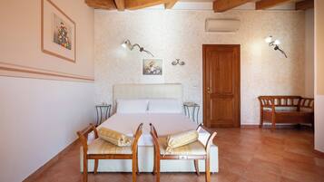 Un dormitorio con cama, sillas de madera, un banco, una puerta y luces fijadas a la pared.