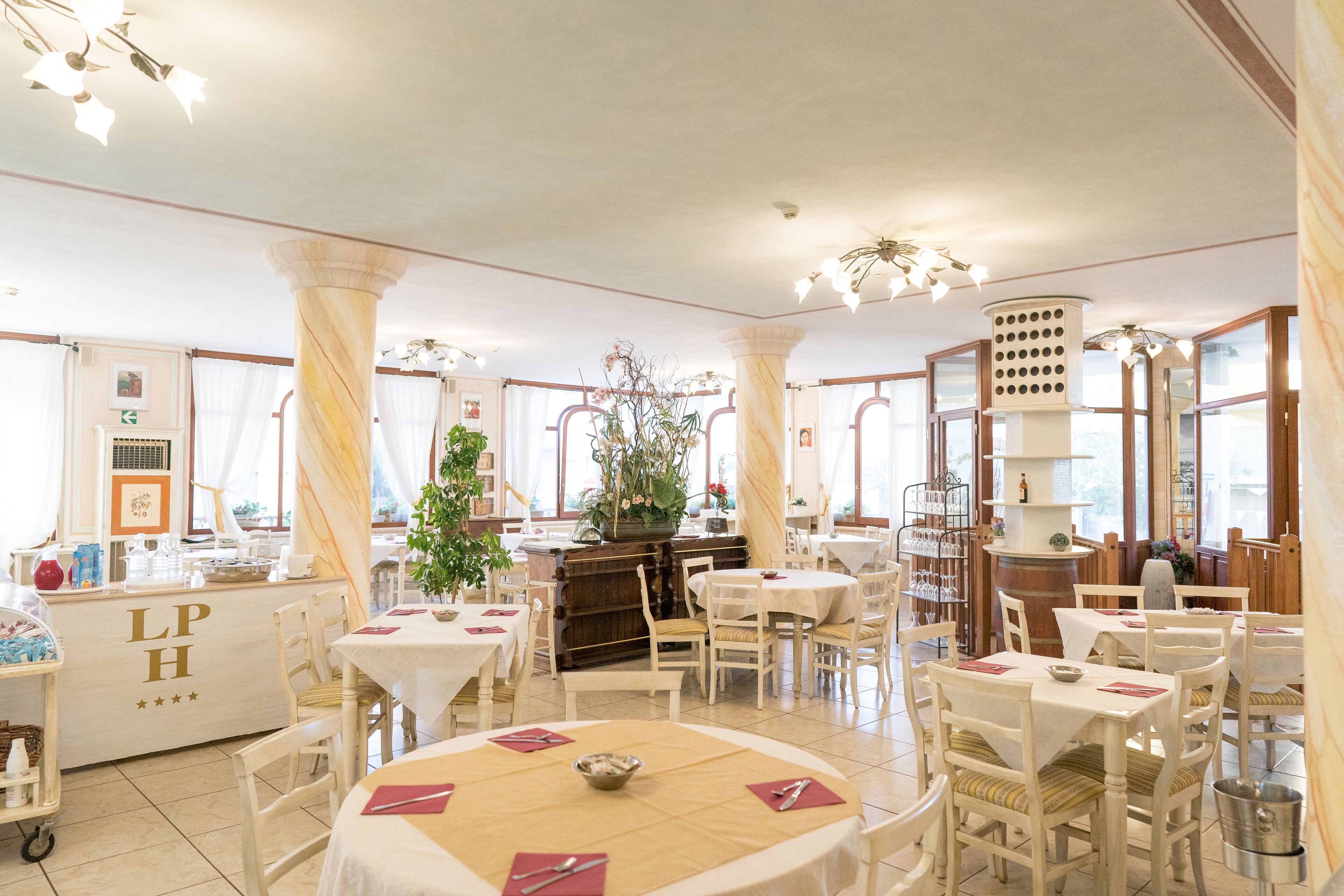 Un amplio comedor con múltiples mesas y sillas, una columna central y una zona de bar con mostrador.