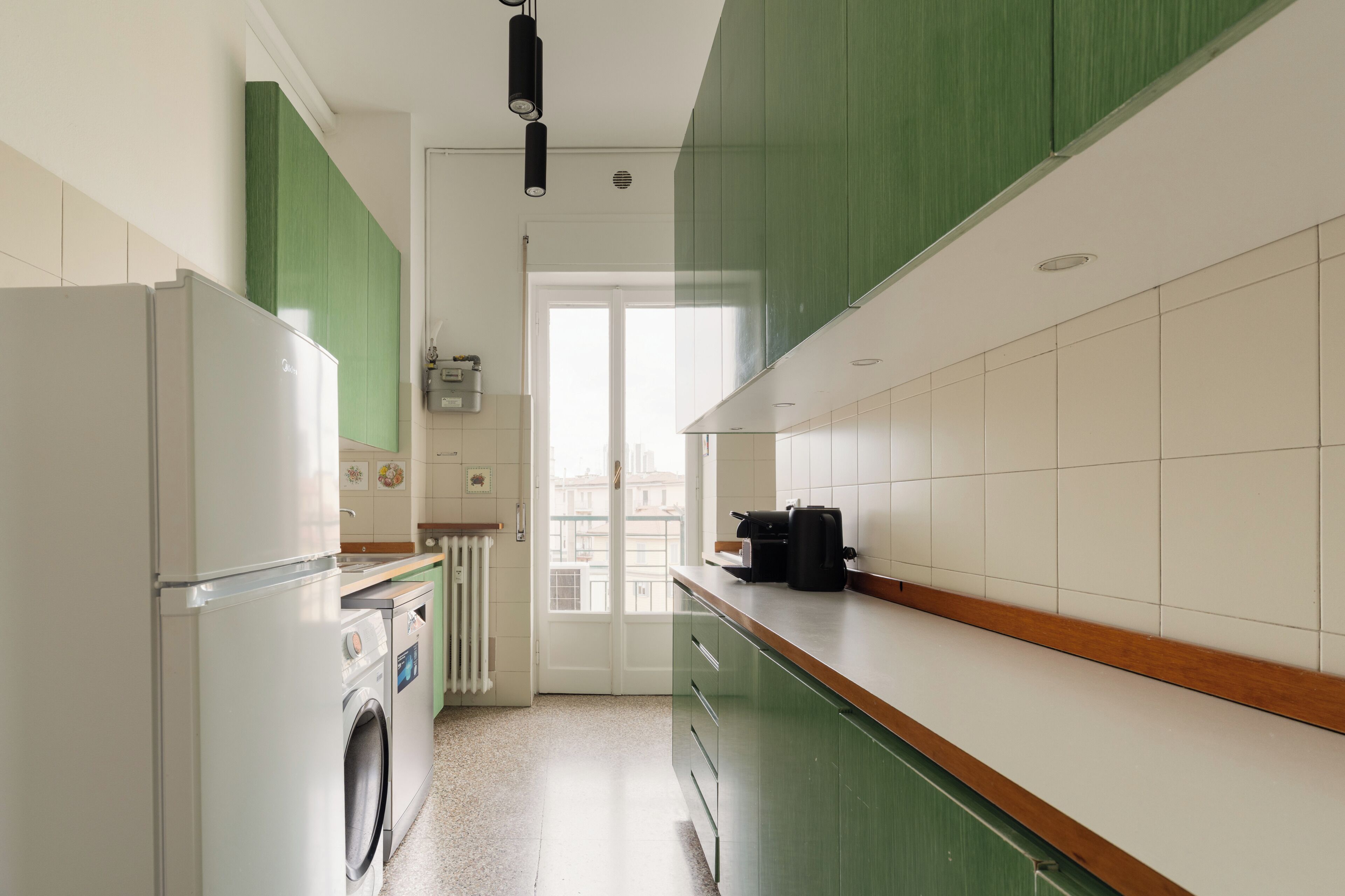 A kitchen with a washing machine, a coffee maker, and a view of the city through a window.