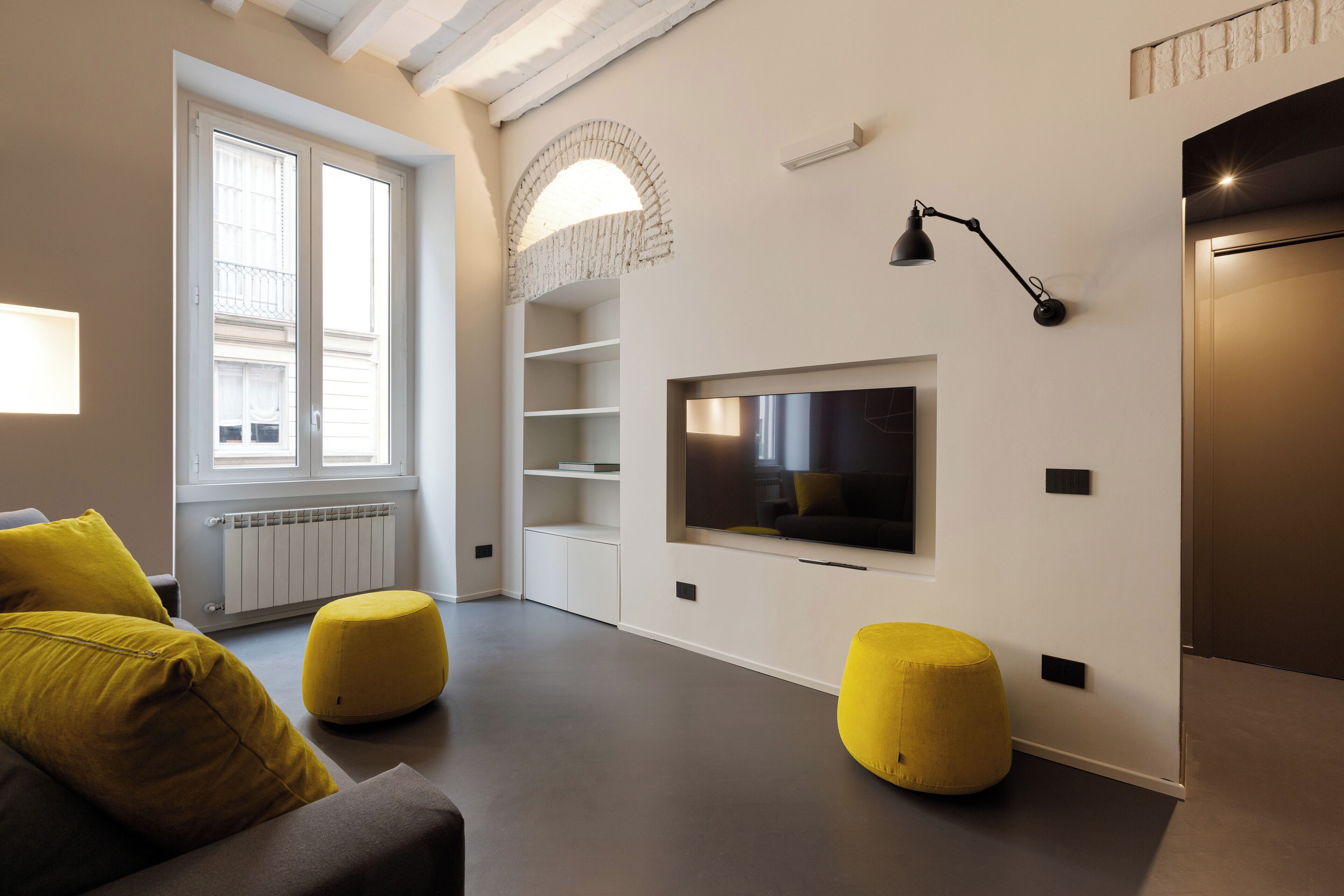 A modern living room with a large window, built-in shelving, a flat-screen TV, and a minimalist design.