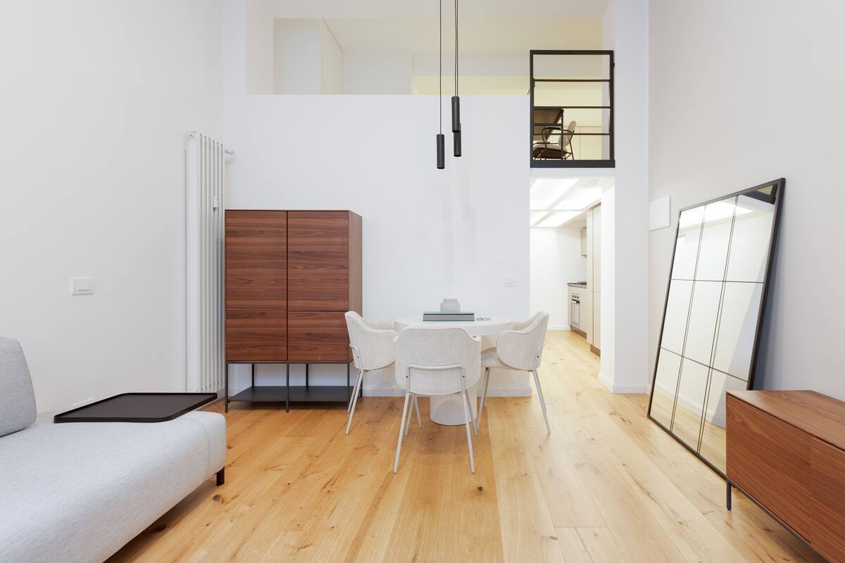 A modern living room with a sofa, dining table with chairs, a wooden cabinet, and a large mirror.