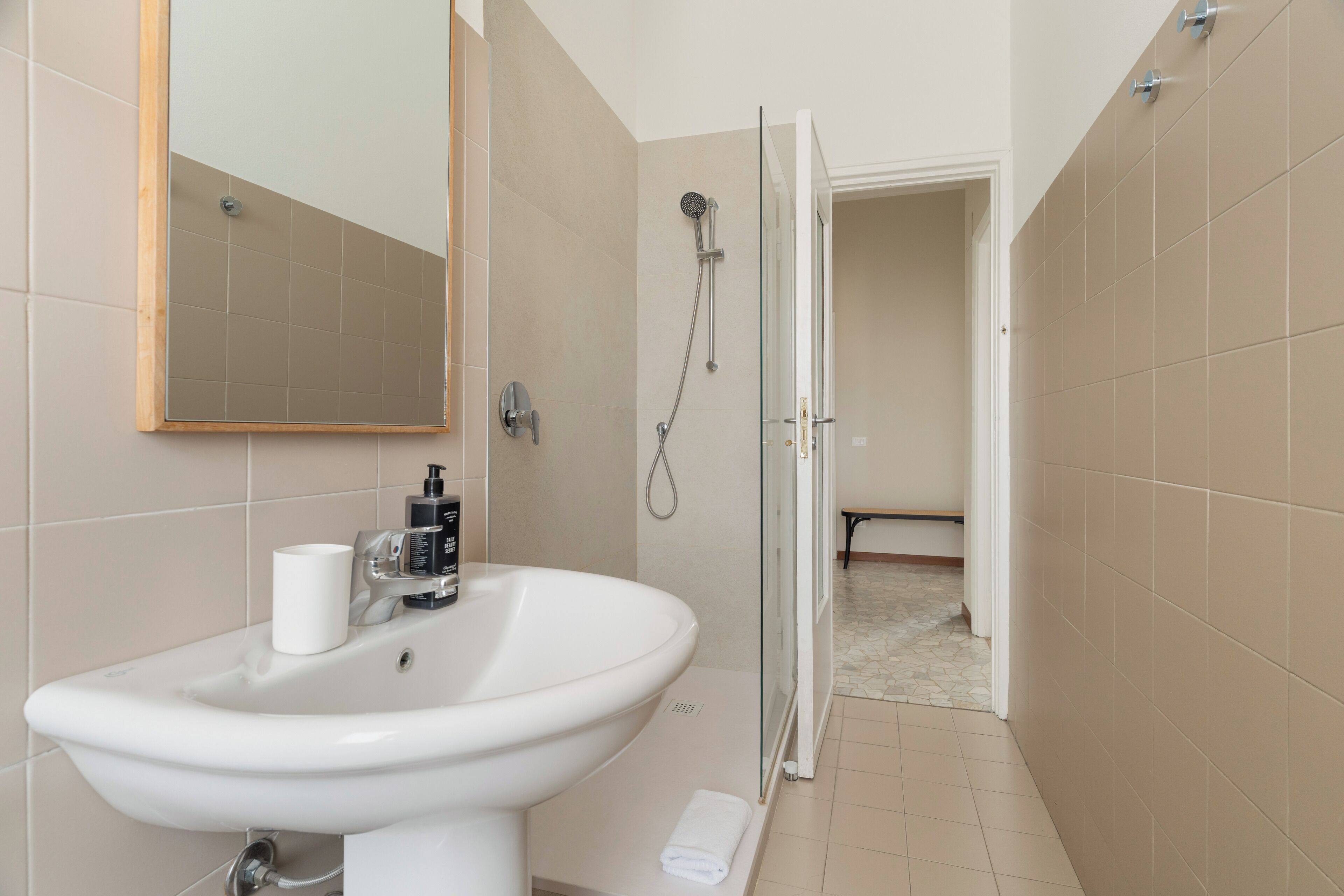 A bathroom with a sink, mirror, shower, and a towel on the floor.