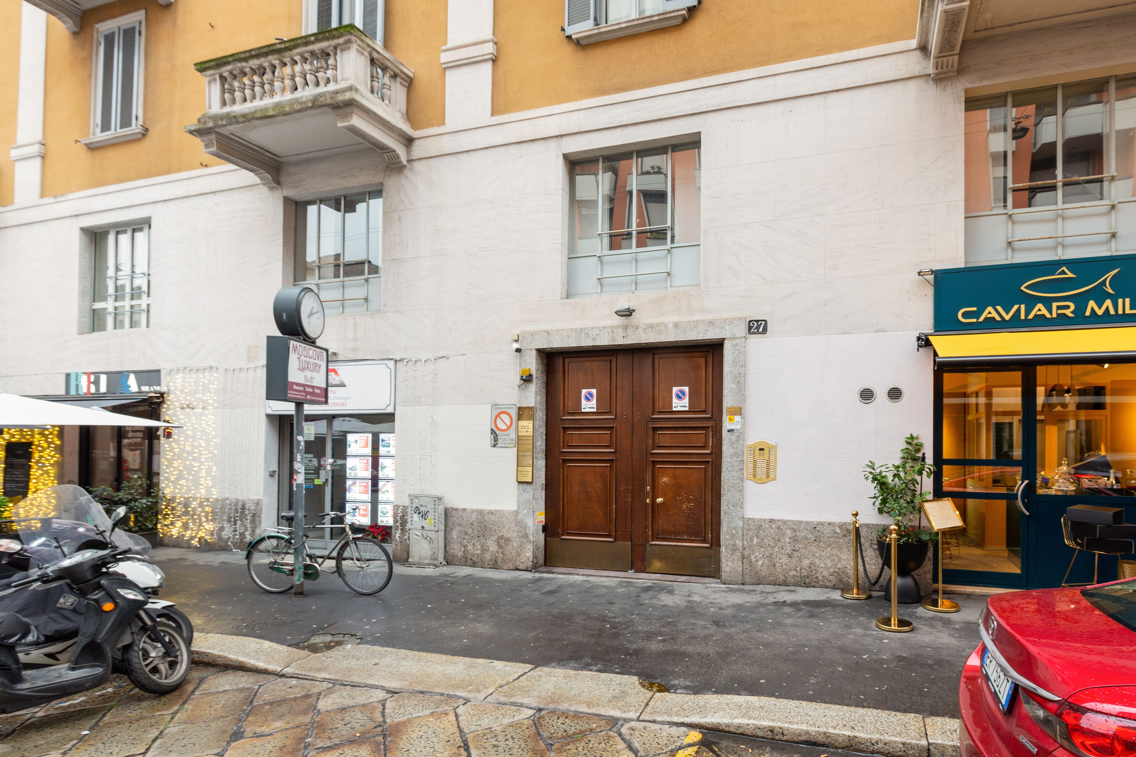 Un edificio con una porta marrone, un cartello con la scritta CAVIER MIL e una bicicletta parcheggiata fuori.