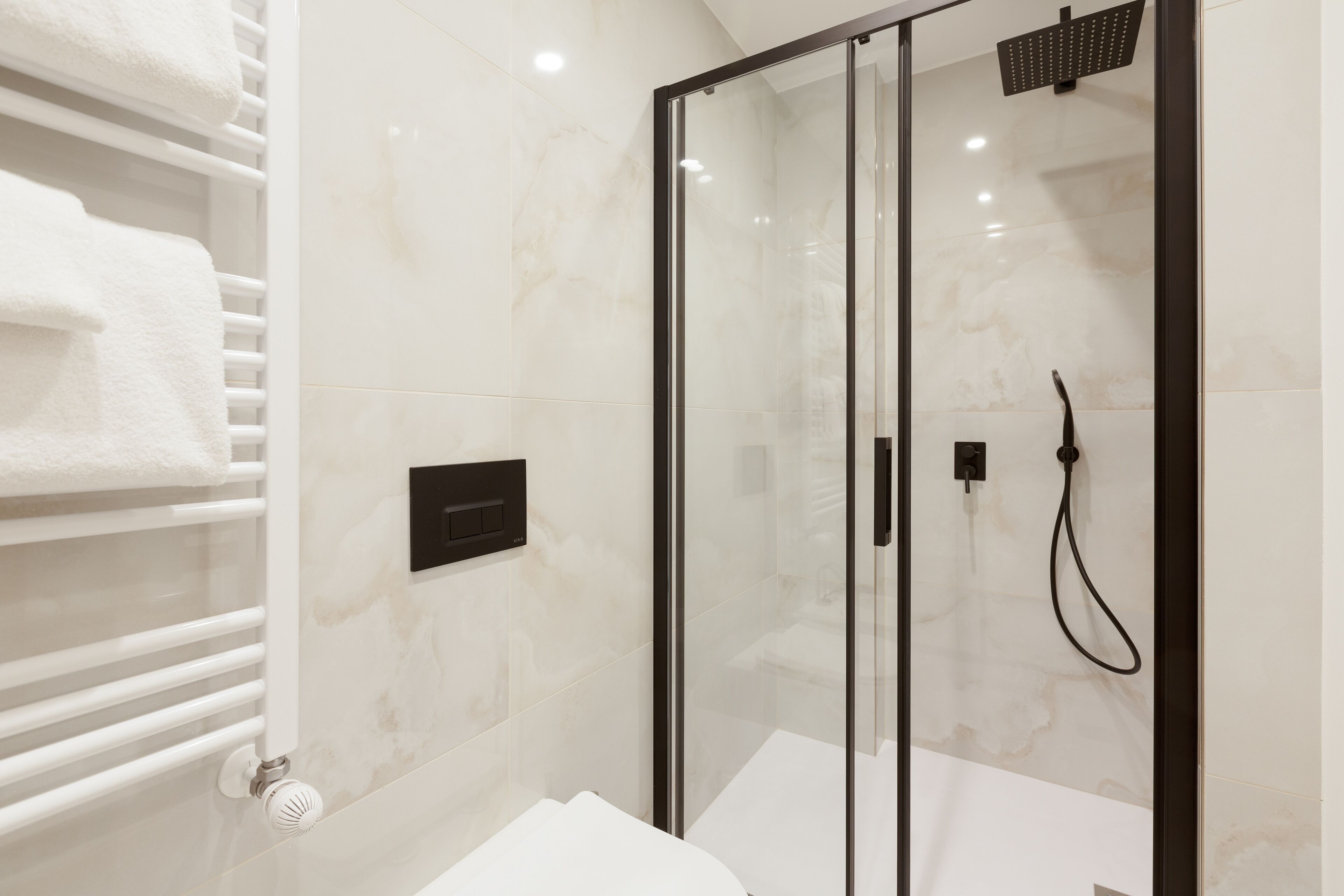Une salle de bain moderne avec une douche à parois de verre, un porte-serviettes blanc et un panneau de commande.